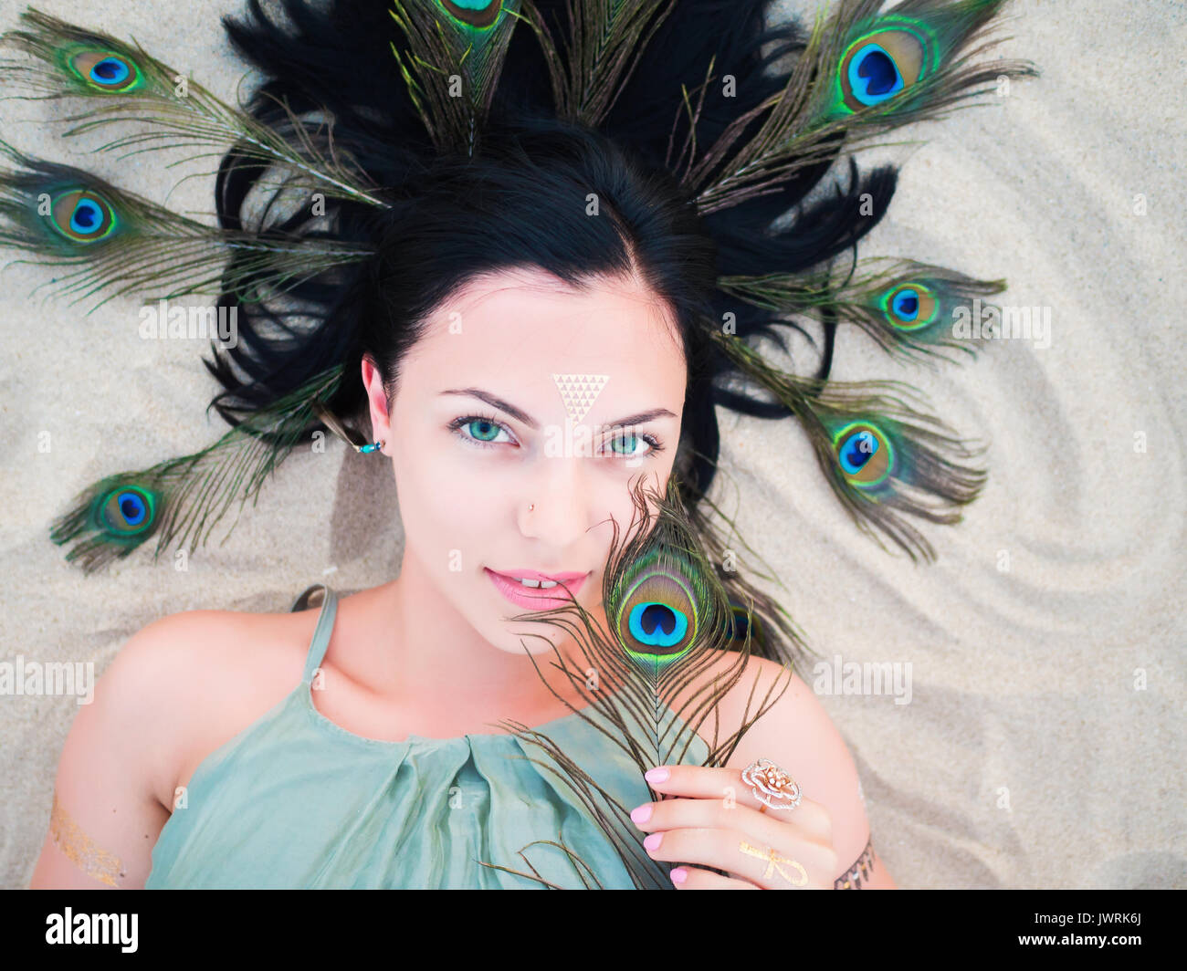 Moda al aire libre Retrato de dama en playa hermosa morenita con flash  tatuajes acostado con plumas de pavo real en el cabello. Estilo boho  gitana, Mujer en verde Fotografía de stock -