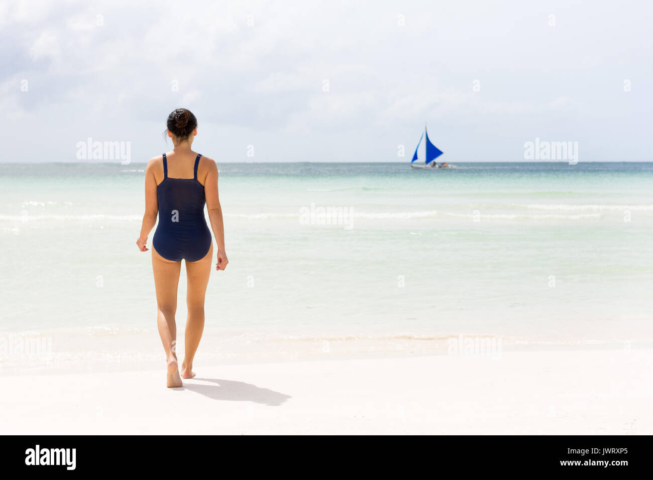 Las hembras jóvenes en bañador camina hacia el claro mar vacío de Boracay beach con velero en el horizonte. Foto de stock