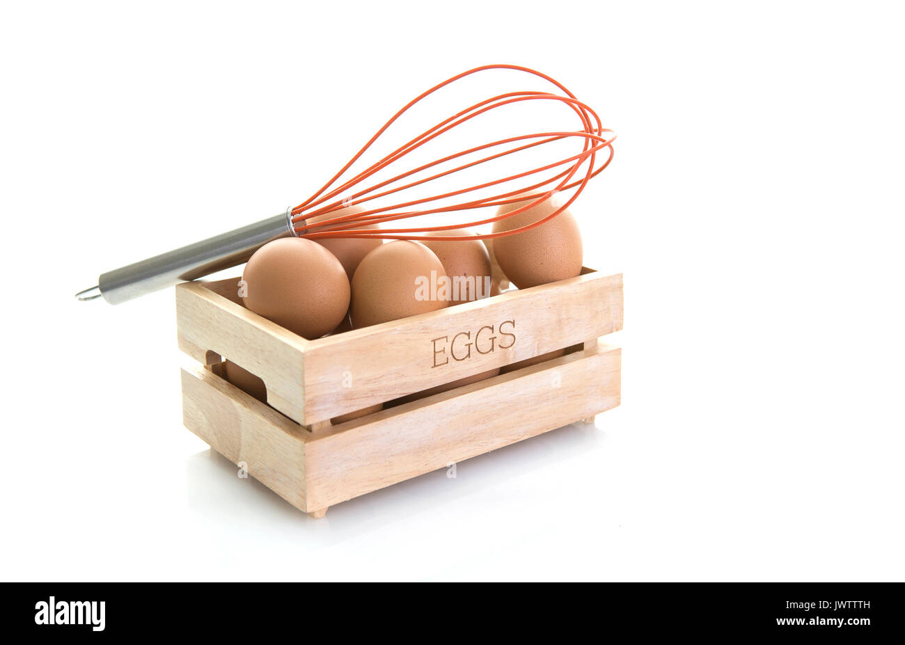 Los huevos en una caja de madera con batidor de huevos de color naranja sobre un fondo blanco. Foto de stock