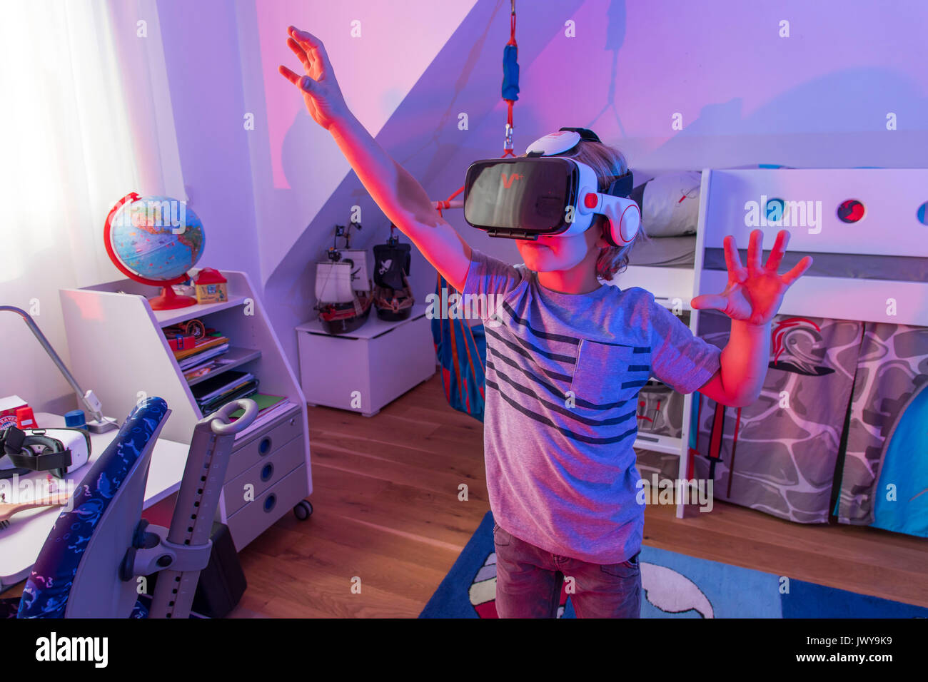 Chico, de 7 años, juega un juego de ordenador en 3-D, con un casco de realidad virtual, en su habitación niños, Foto de stock