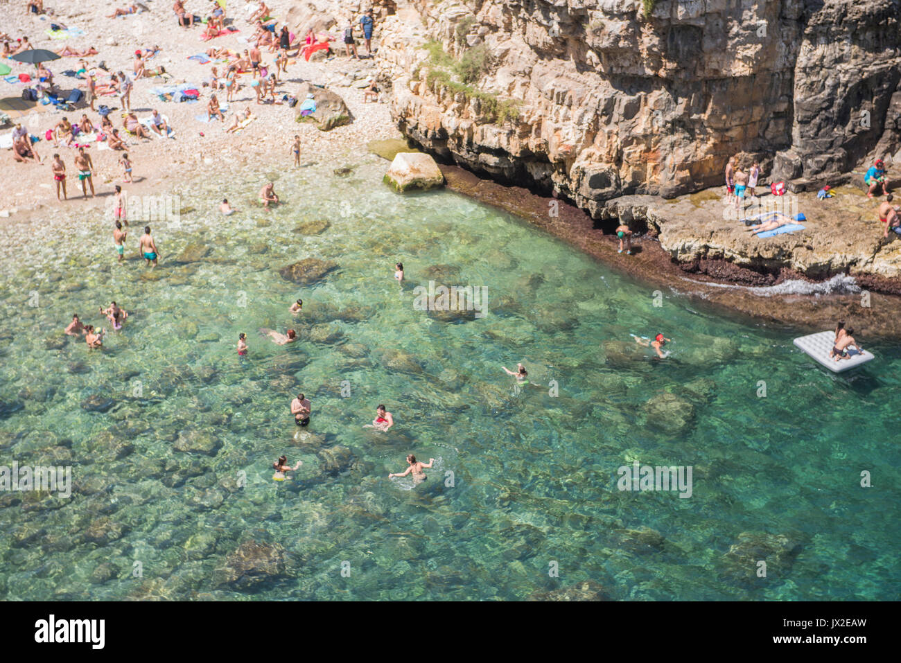 Los nadadores Wade en el espectacular océano turquesa en Polignano a Mare. La playa también es el sitio de la reunión anual de la Red Bull cliff-Competición de buceo. Foto de stock