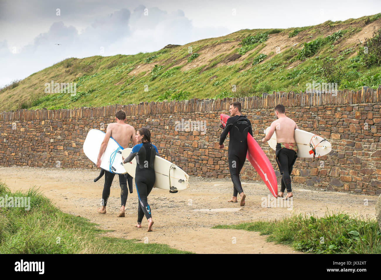 Surf en el Reino Unido. Cuatro surfers llevando sus tablas de surf a lo largo de un sendero en Newquay, Cornwall. Foto de stock