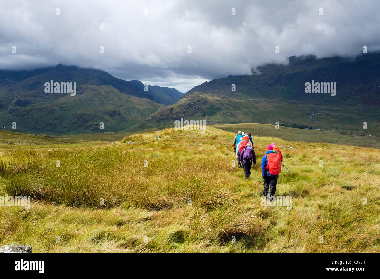 Grupo de excursionistas y Cribau Carnedd caminando hacia abajo a Pen Y Gwryd en sol después de las lluvias en las montañas del Parque Nacional de Snowdonia. Gales UK Foto de stock