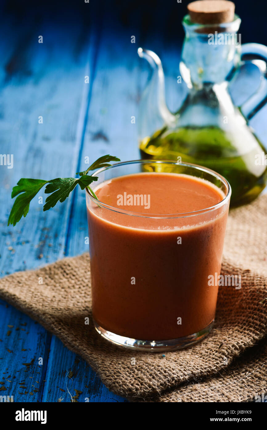 Primer plano de un vaso con refrescante gazpacho, la sopa de tomate fría  típica española, en una rústica mesa de madera azul, y un vidrio cruet con  aceite de oliva Fotografía de