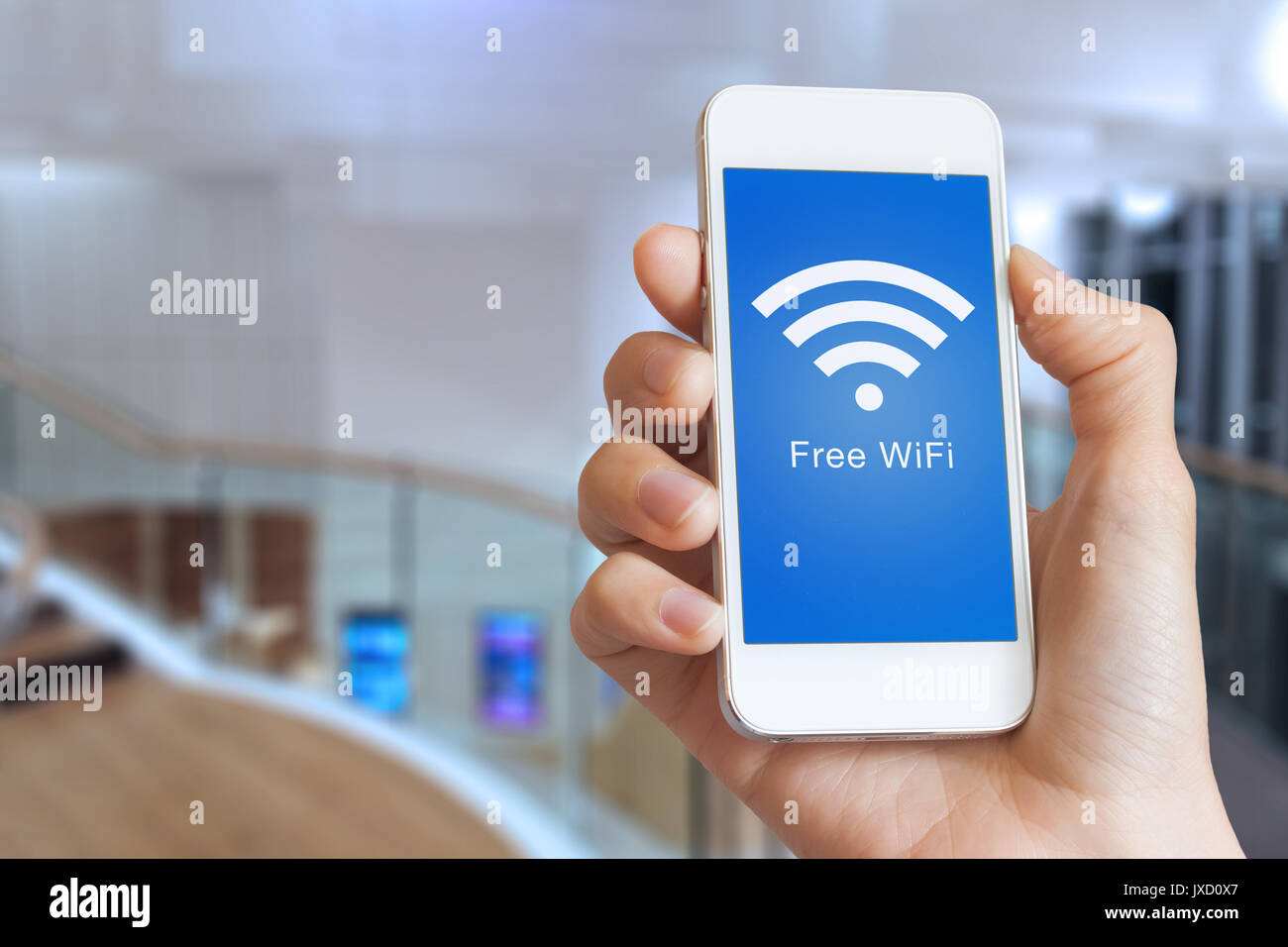 Close-up de mano sujetando smartphone con WiFi hotspot gratis icono en la pantalla para conectarse a internet inalámbrico, interiores de edificios públicos en segundo plano. Foto de stock