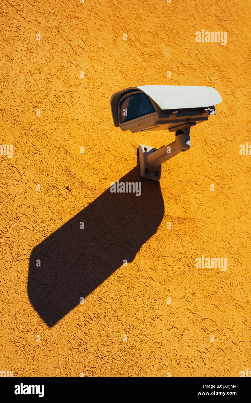 Cámara de seguridad en la pared amarilla, tecnología moderna de vigilancia sobre la construcción de la fachada con sombra Foto de stock