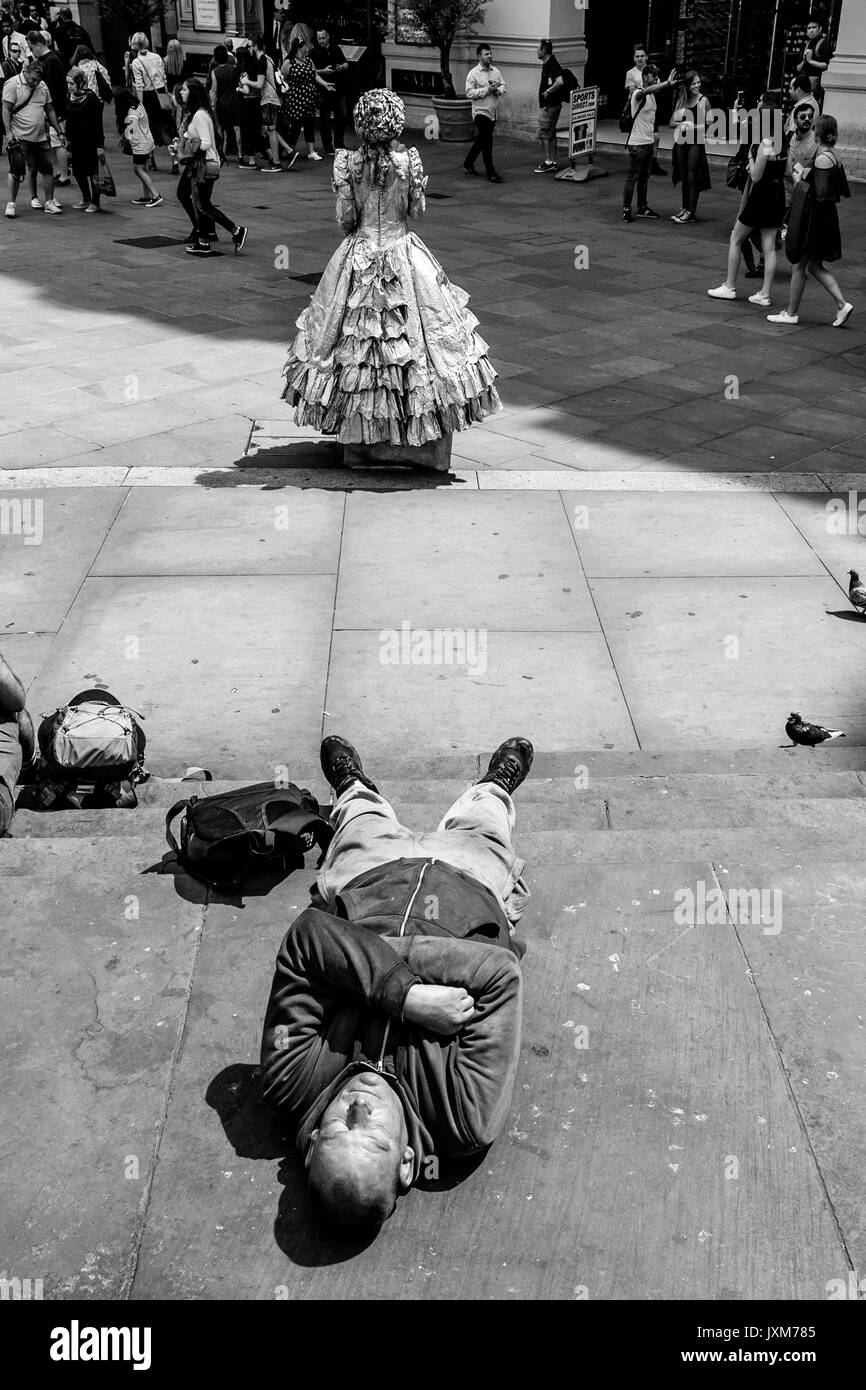 Un hombre dormido sobre los pasos de la Estatua de Eros, Piccadilly Circus, Londres, Reino Unido. Foto de stock