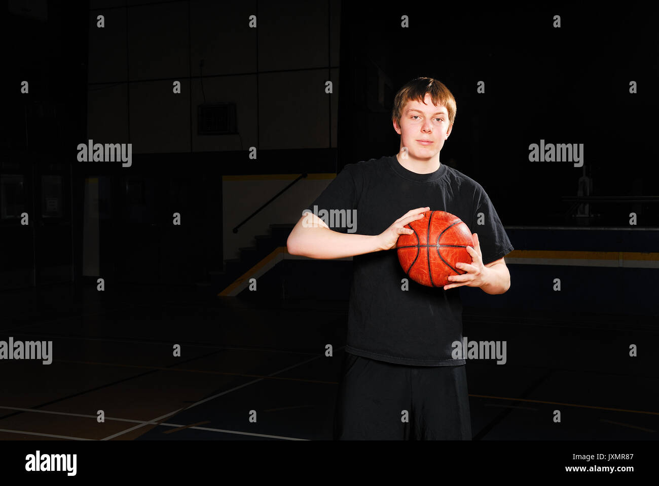 El jugador de baloncesto solo en un gimnasio de highschool oscuro Foto de stock