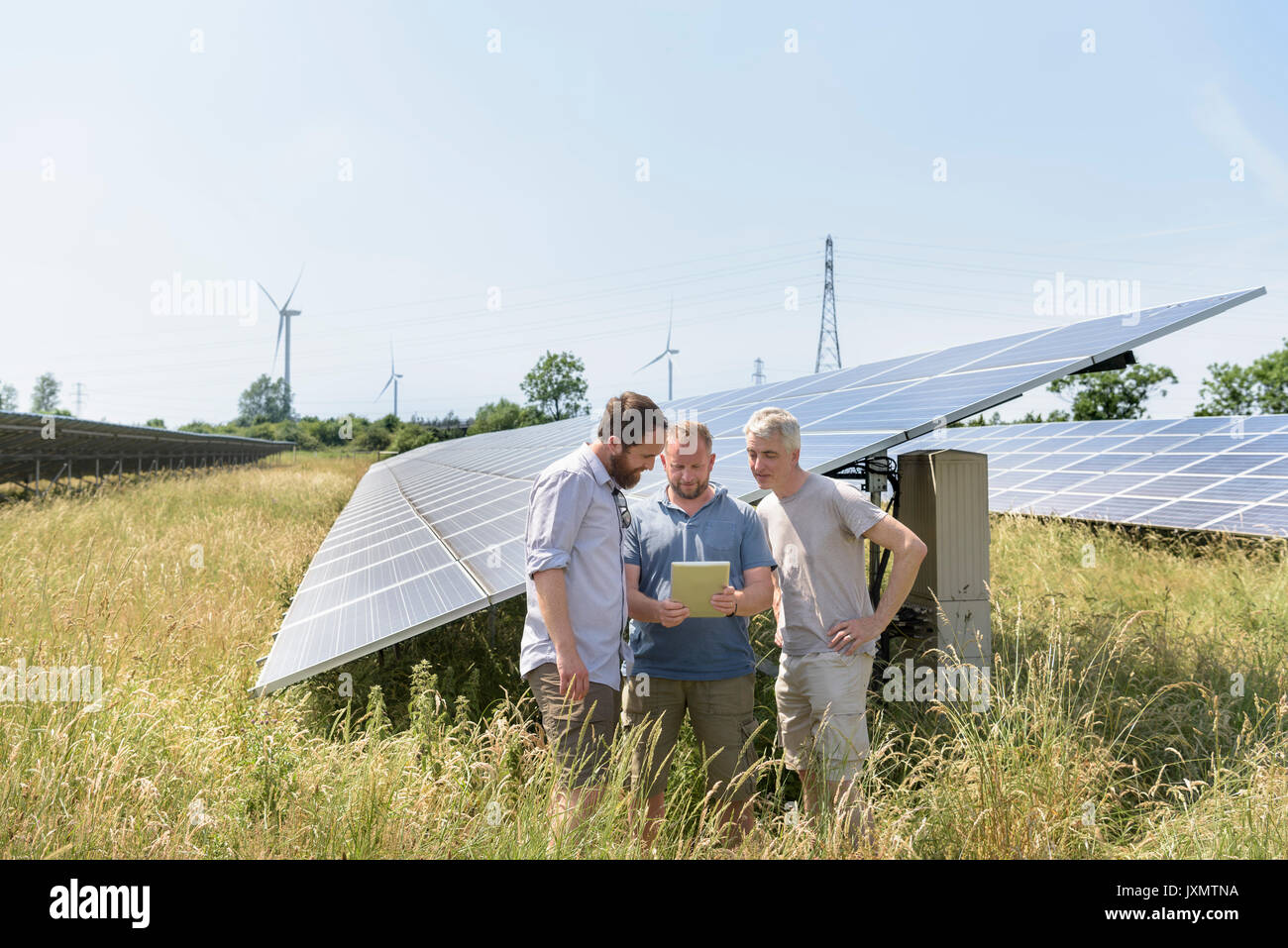 Los miembros de la comunidad local mediante tableta digital app para mirar el rendimiento energético de la granja solar Foto de stock