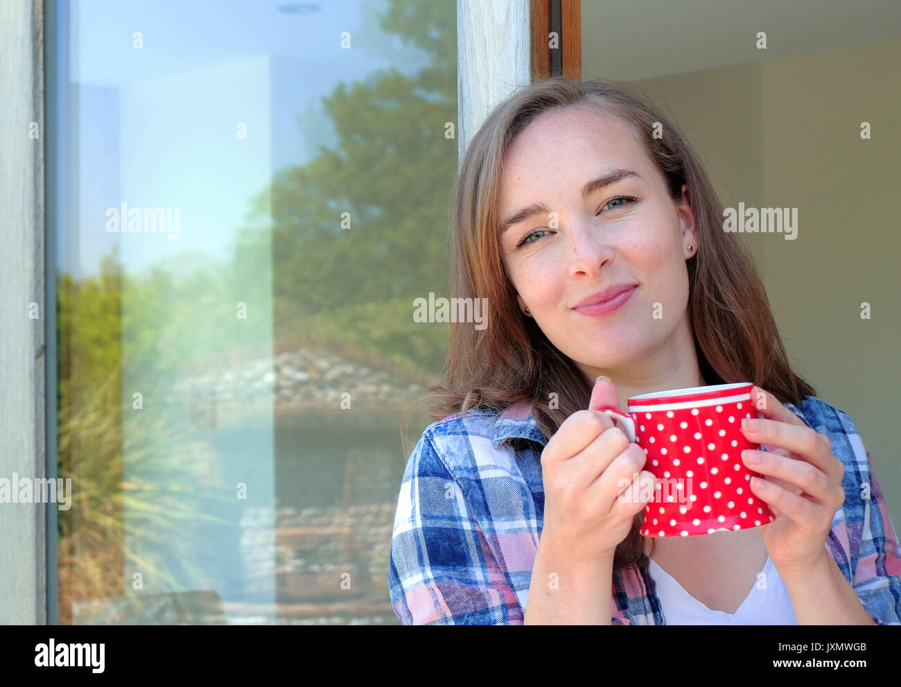 Retrato de mujer joven celebración taza de café por la puerta del patio Foto de stock