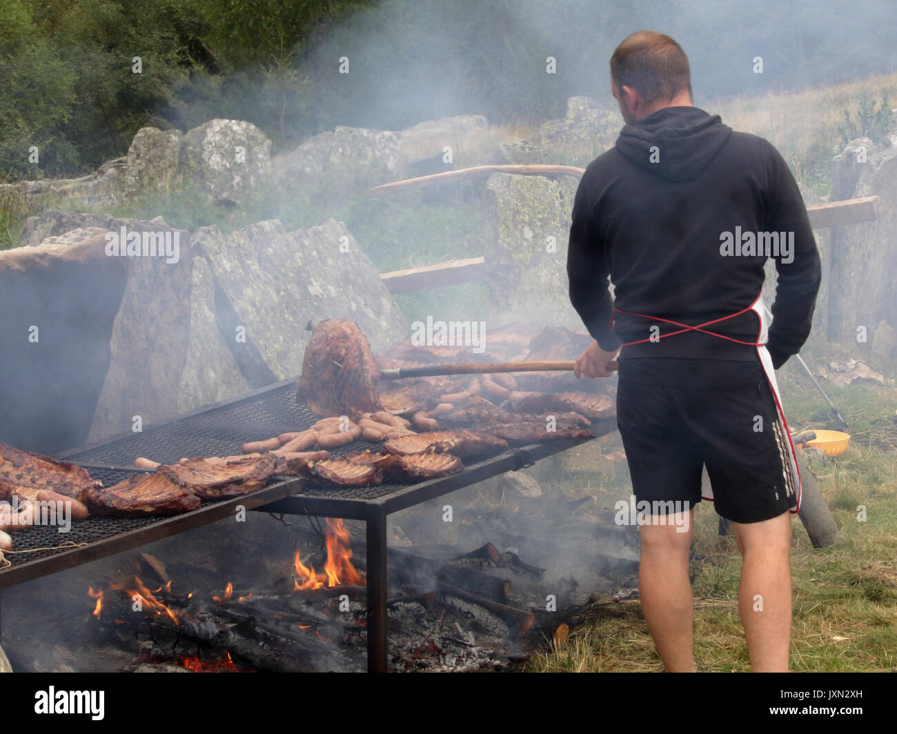 Un hombre asar carne y fumar en una hoguera de leña y carbón durante una barbacoa en el valle Vigezzo, Alpes del norte de Italia Foto de stock