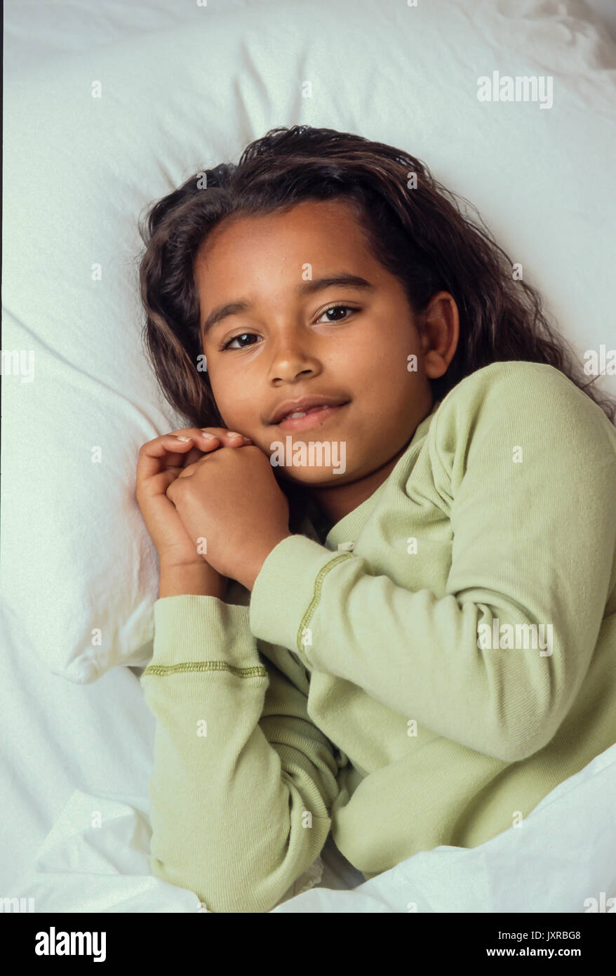 A la hora de acostarse para niña 7-10 años en cama dispuesta a orar y a dormir/Caucásico Afroamericano Foto de stock