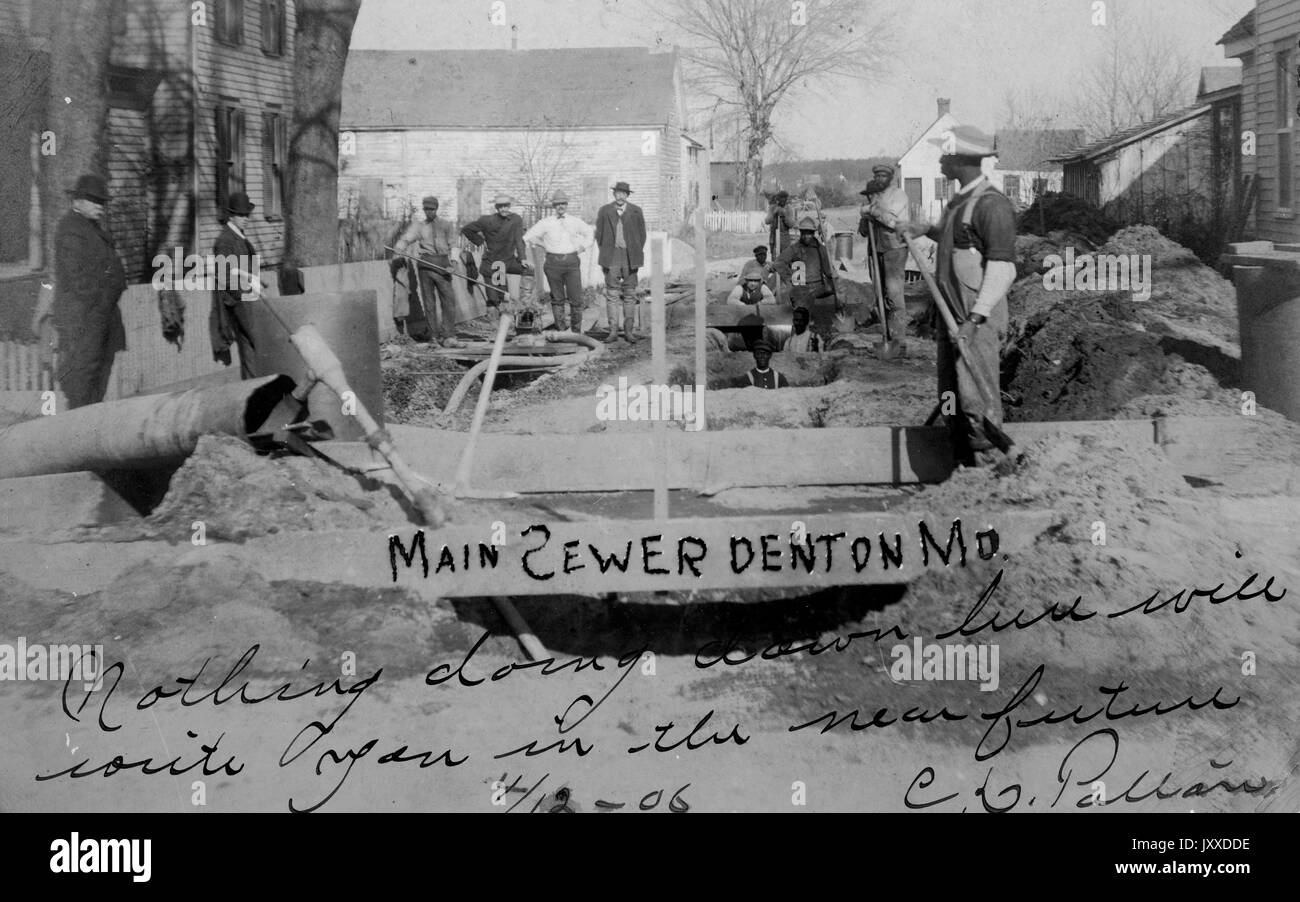 Un grupo de trabajadores estadounidenses con expresiones neutrales se encuentra fuera con herramientas y equipo, trabajando en el sistema de alcantarillado de una ciudad americana, probablemente Denton, Maryland, 1915. Foto de stock