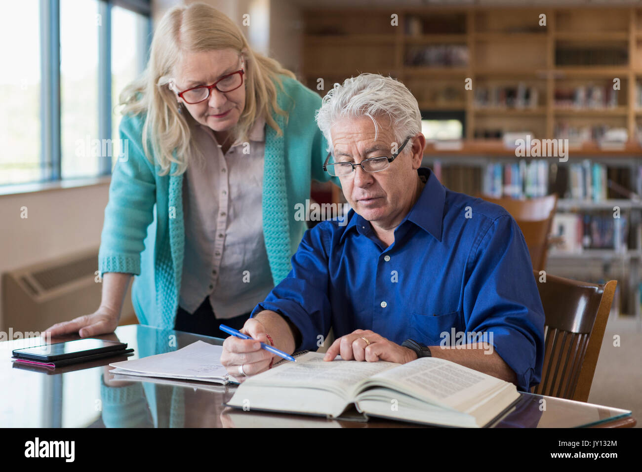 Mujer de edad ayudando al hombre libro de lectura en la biblioteca Foto de stock