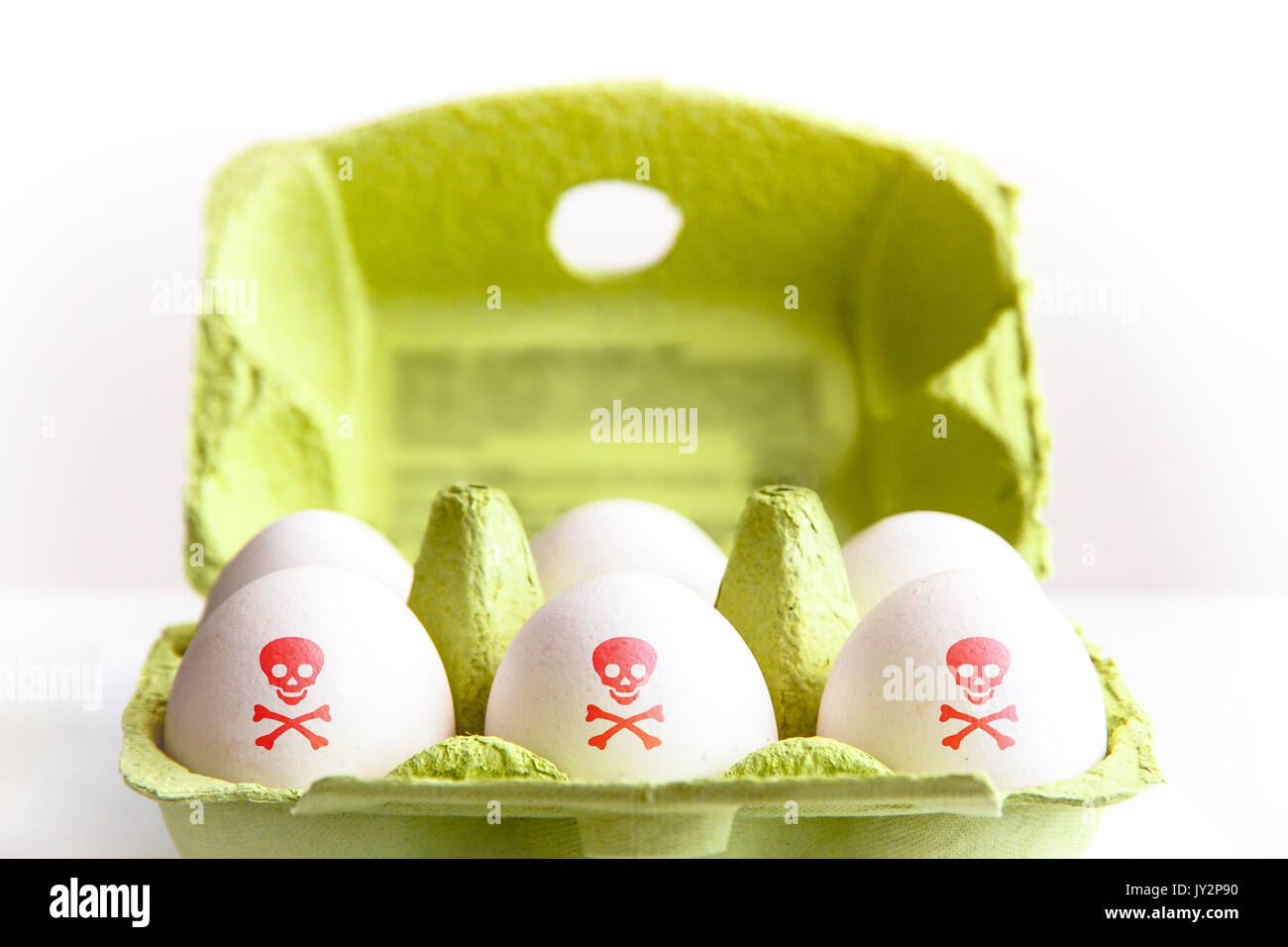 Huevos en un paquete de papel verde con los huevos pintados de color rojo con un símbolo de riesgo tóxico de cráneo y huesos. Concepto de contaminación alimentaria huevo escándalo. Foto de stock