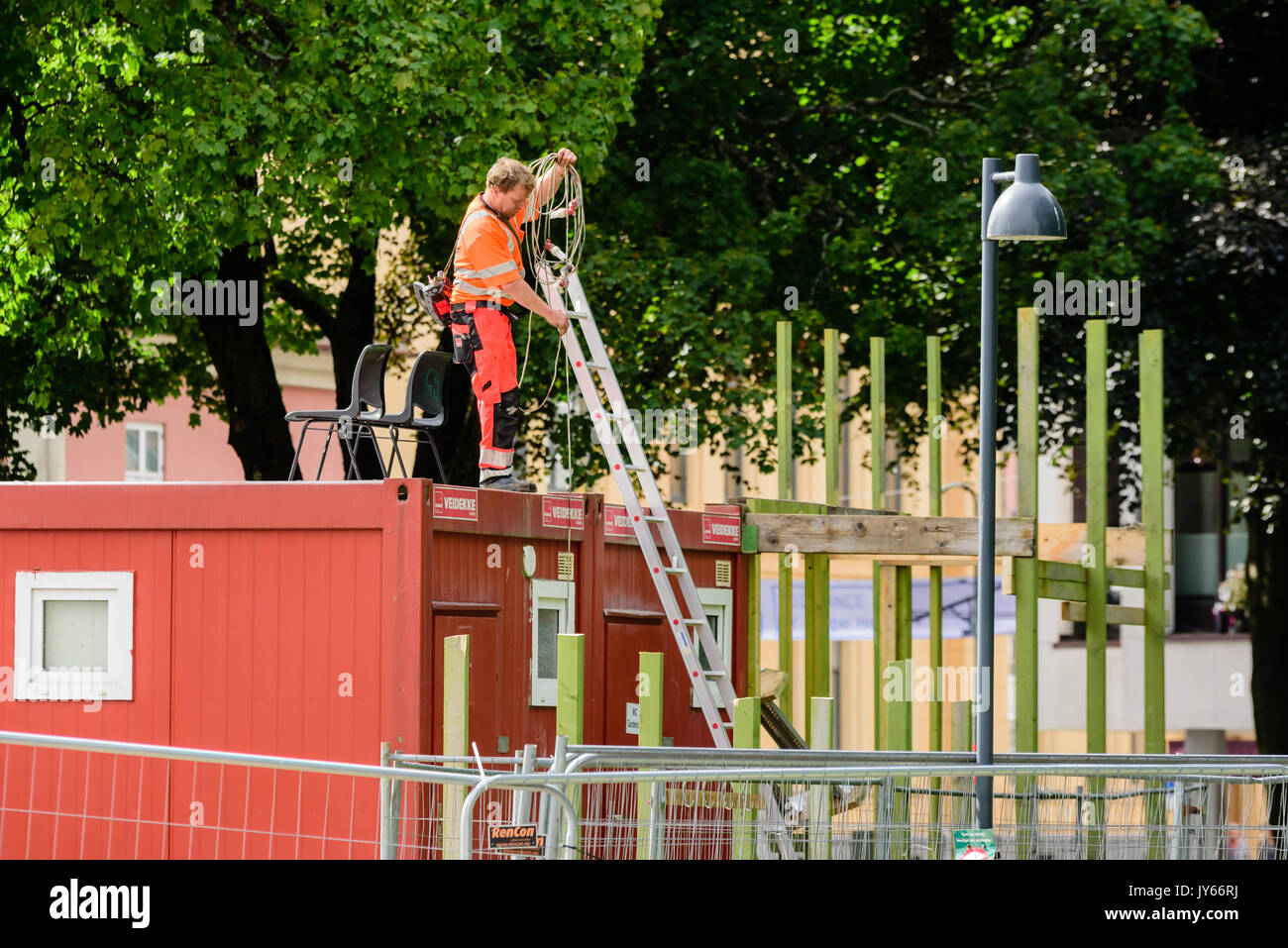 Kristiansand, Noruega - Agosto 1, 2017: Documental de la vida cotidiana en la ciudad. Trabajador de la construcción en toolshed bobinado del techo de un cable eléctrico. Ladde Foto de stock