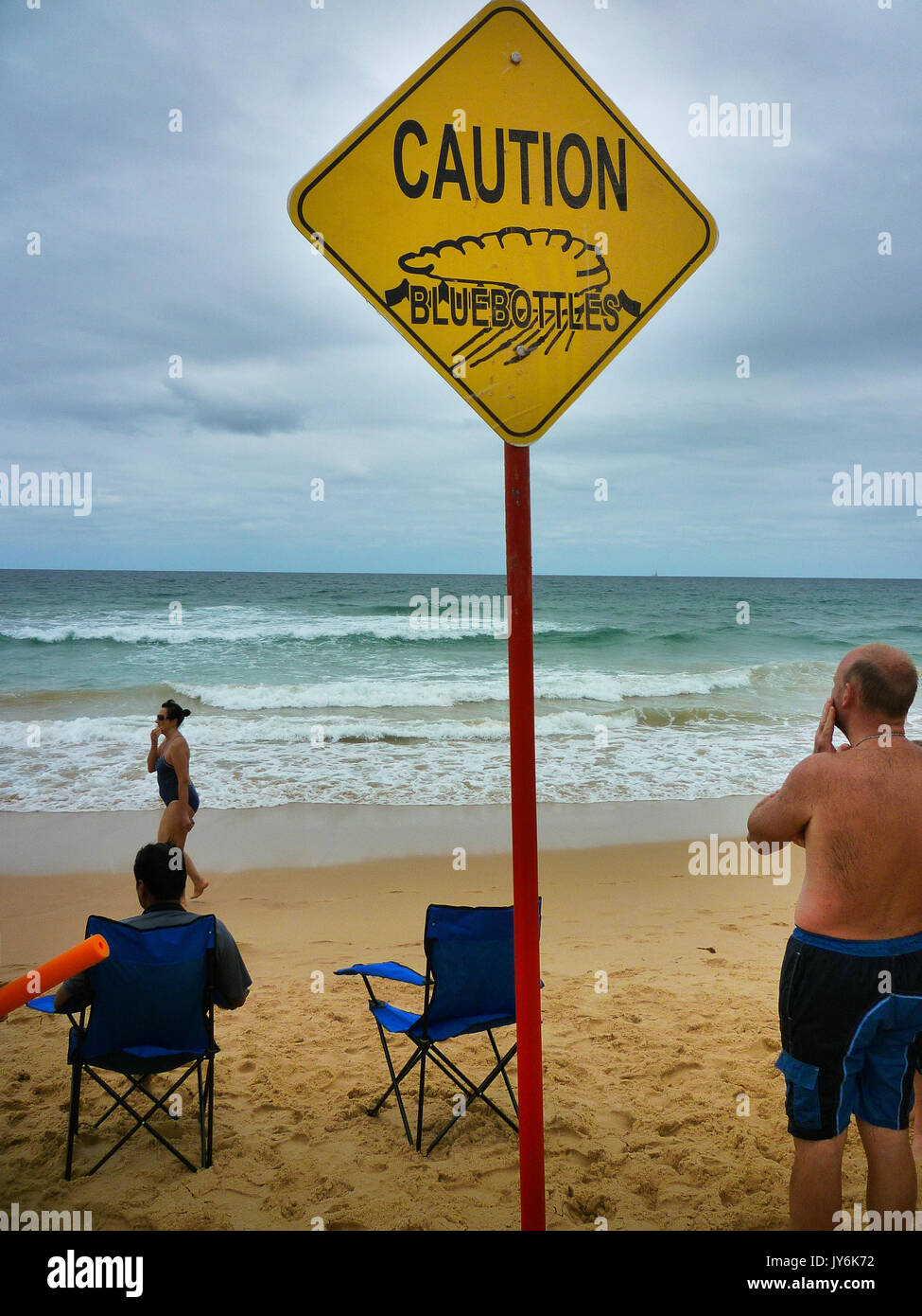 Un hombre de pie junto a un signo de advertencia de bluebottles relojes del mar en Australia Foto de stock