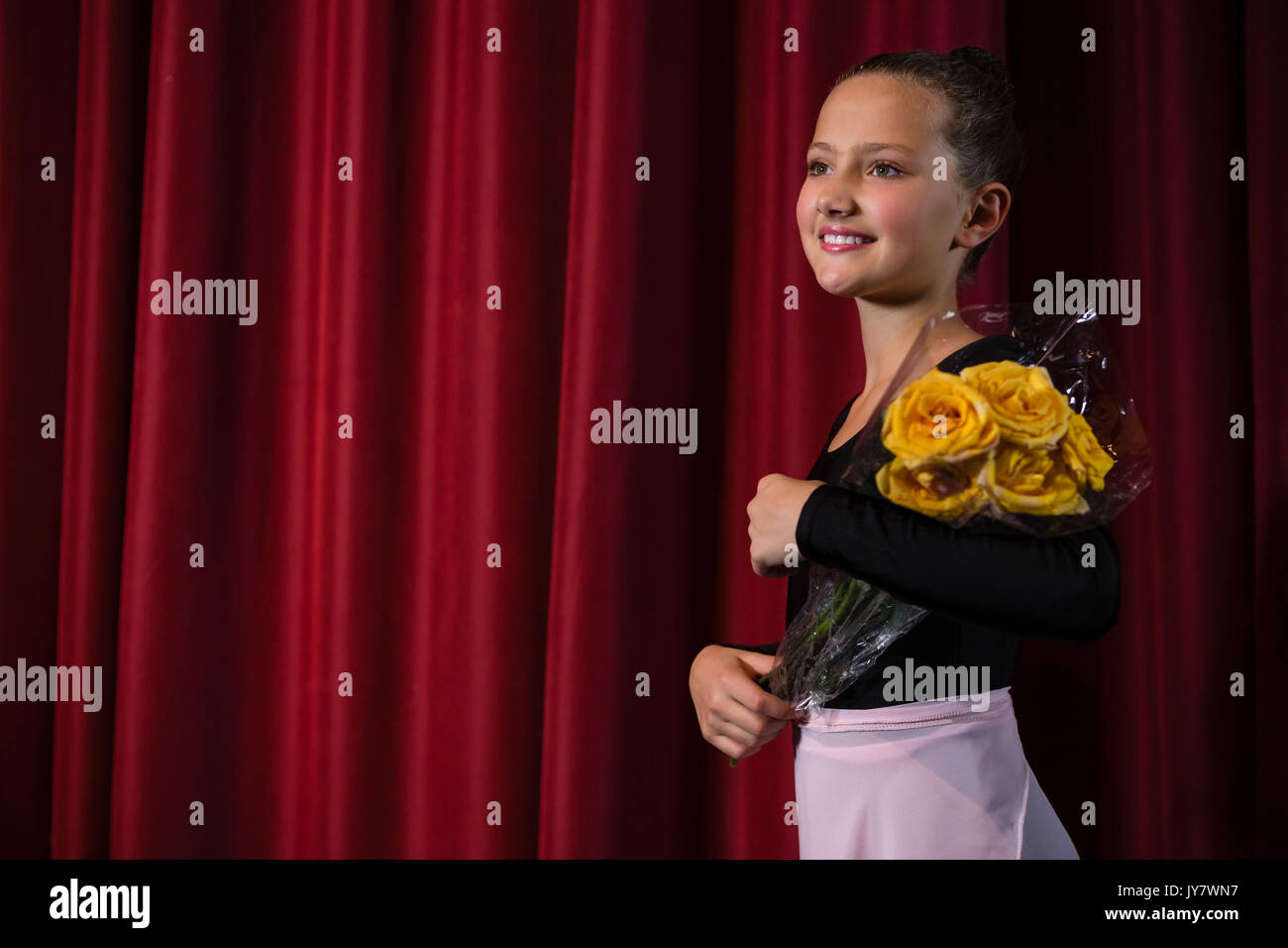 Feliz bailarina posando con ramo de flores en el escenario de teatro