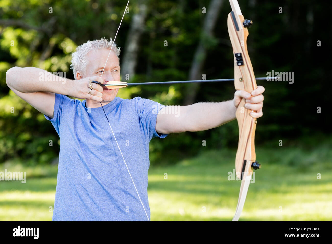 Atleta Masculino apuntando con arco y flechas en el bosque Foto de stock