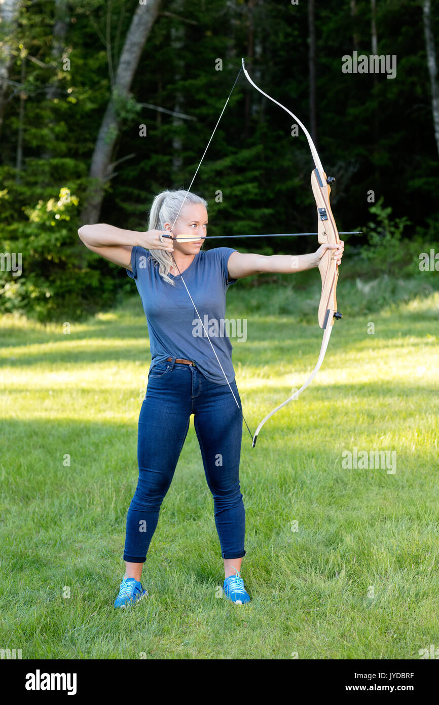 Seguros de mujer apuntando con arco y flechas en el bosque Foto de stock