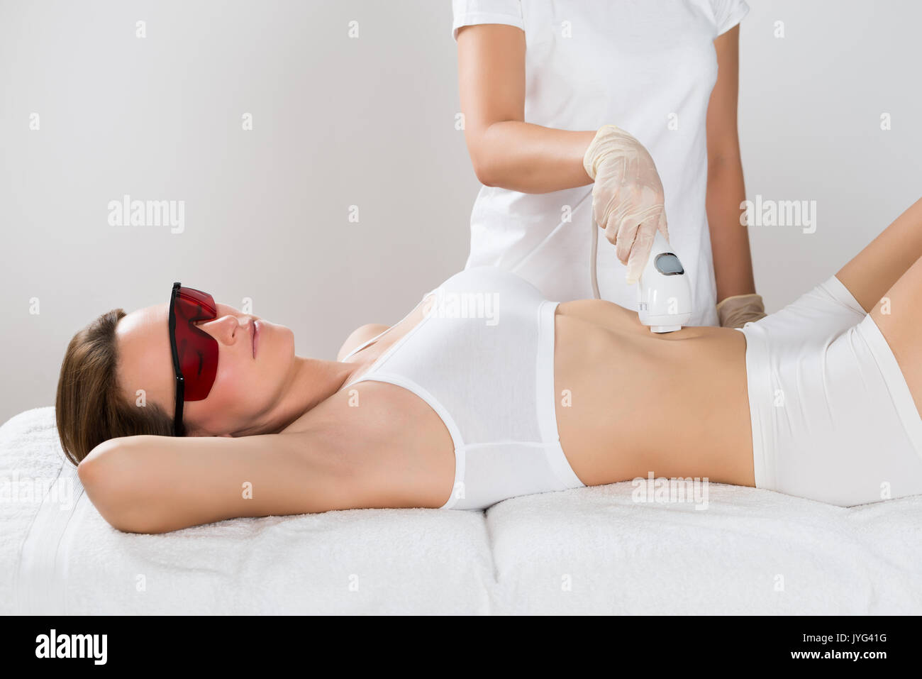 Mujer joven tumbado en la cama recibiendo tratamiento con láser de depilación sobre barriga Foto de stock