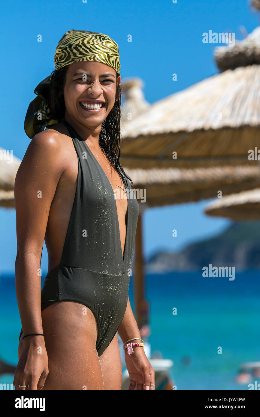 Retrato de sonriente joven mujer árabe en traje de baño, vestido con  pañuelo de seda y mirando a la cámara, sombras contra el sol y el mar azul  Fotografía de stock -