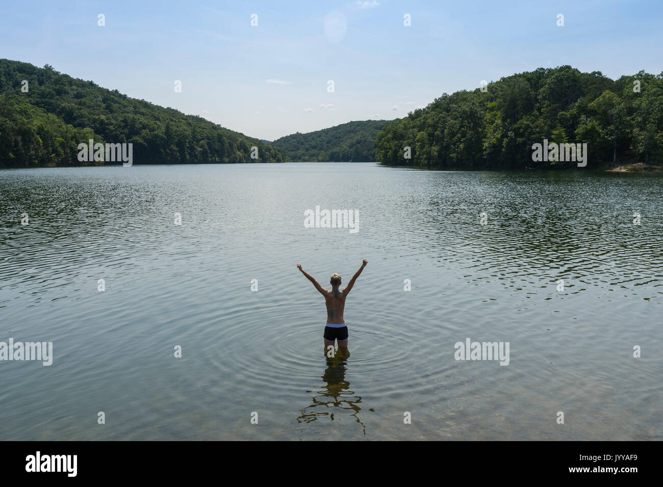 Mujer de pie con los brazos levantados en el lago Foto de stock