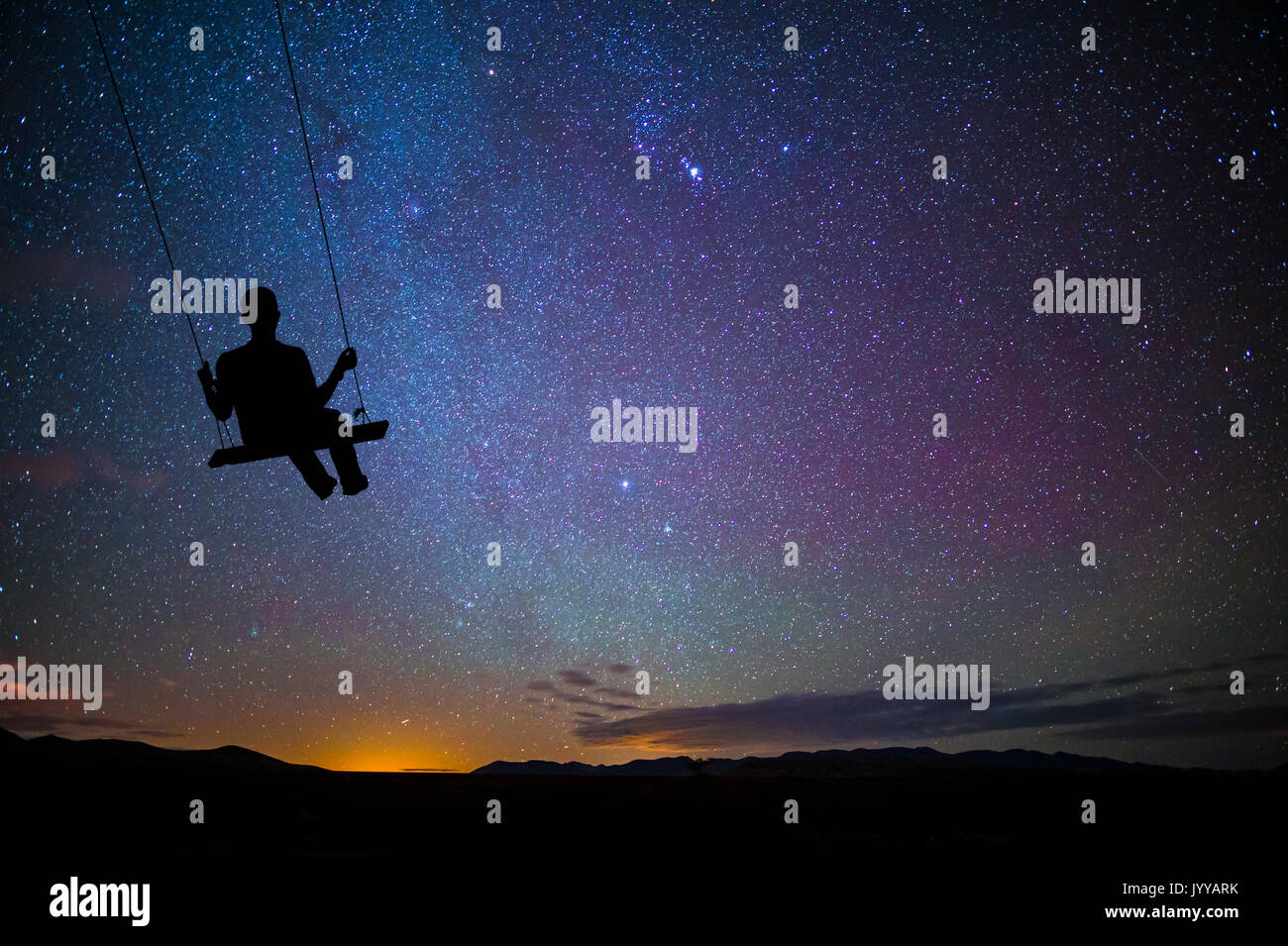 Niño en el columpio balanceándose con las estrellas en la noche Foto de stock