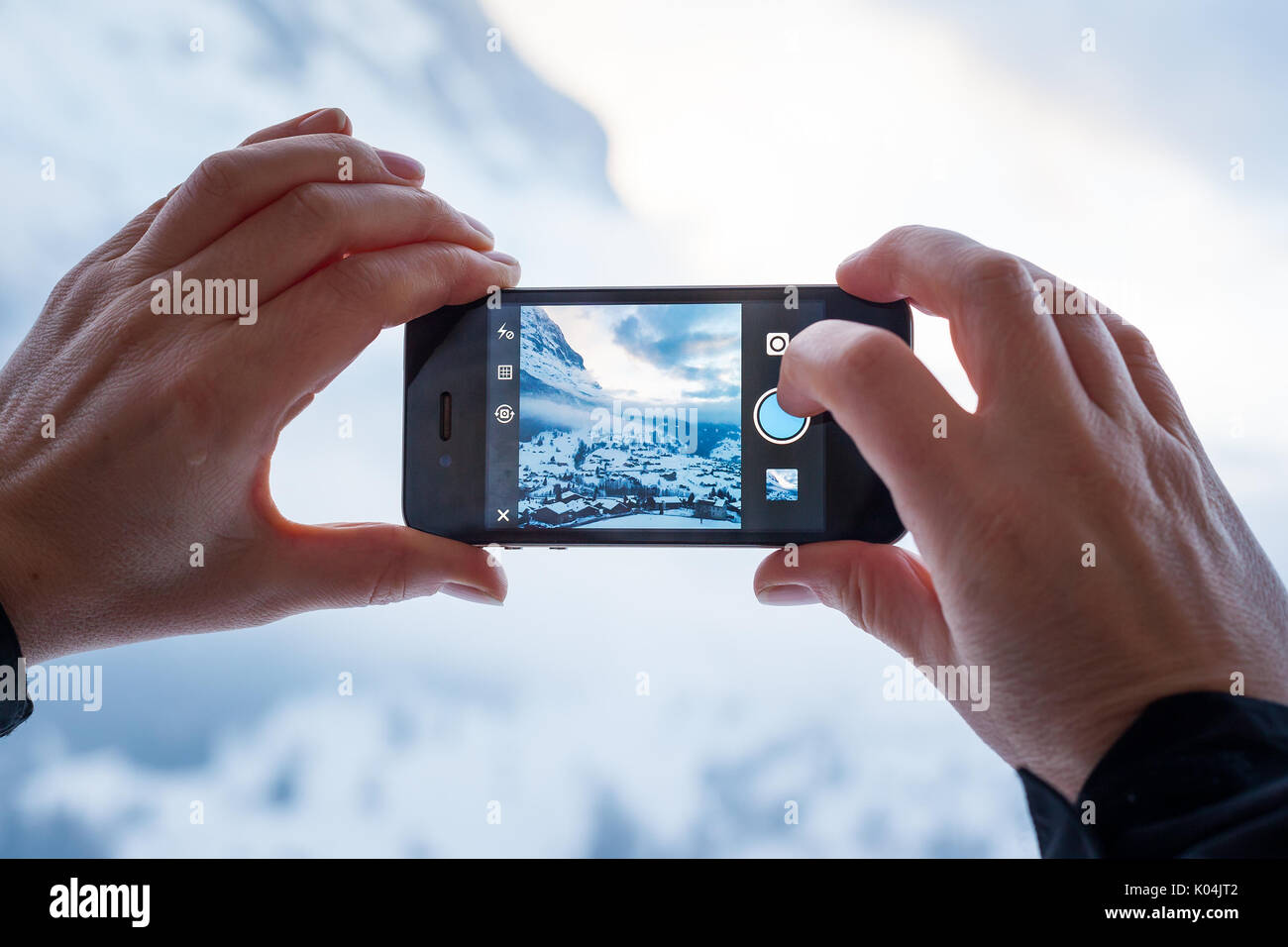 GRINDELWALD, Suiza - febrero 4, 2014: la mujer toma una fotografía de las montañas mediante la aplicación Instagram en un Apple iPhone. Instagram permite a los usuarios Foto de stock