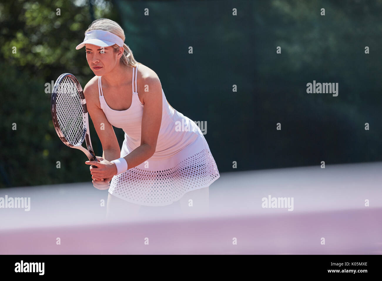 Centrado joven jugador de tenis femenino listo, celebración de raqueta de tenis en la cancha de tenis soleada Foto de stock