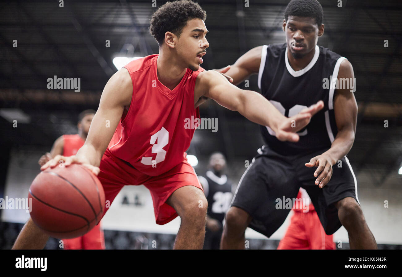 Joven jugador de baloncesto masculino haces botar el balón, protegiendo de defender en juego de baloncesto Foto de stock