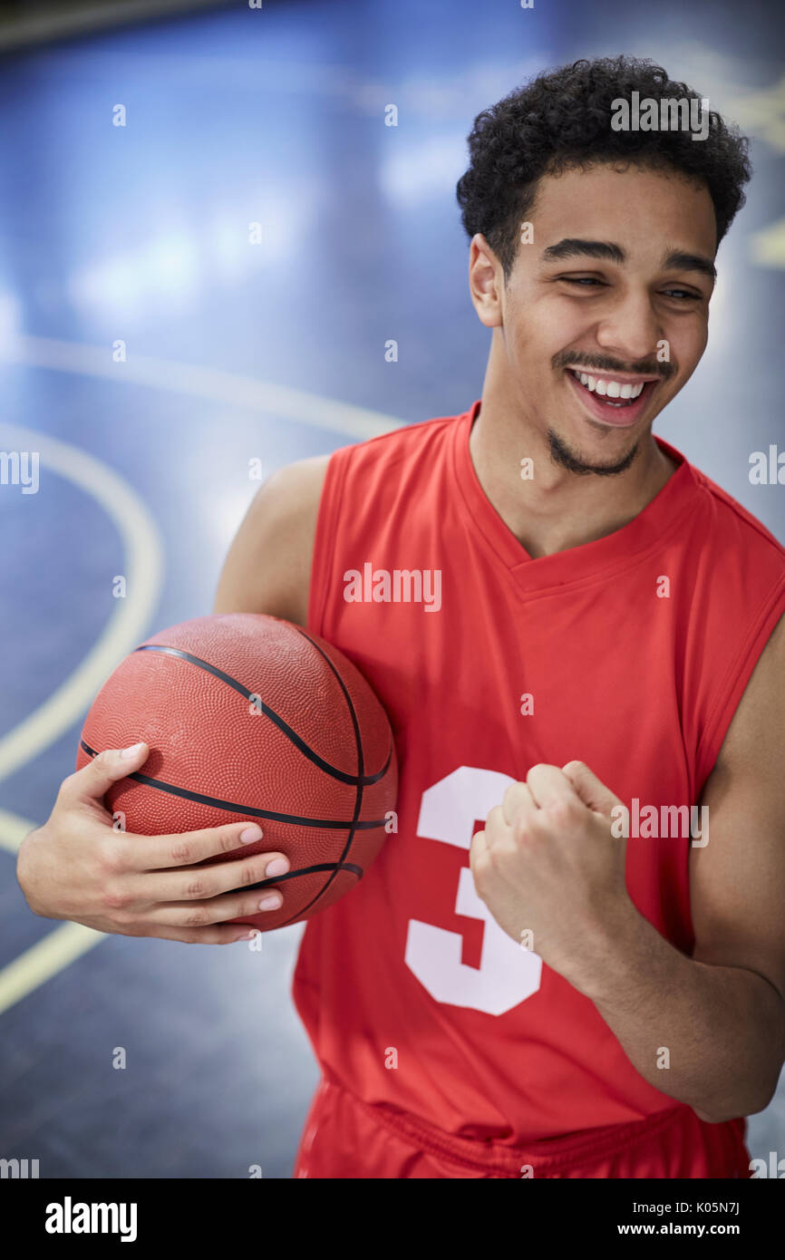 Retrato seguro, feliz, joven jugador de baloncesto masculino gesticulando, celebrando la victoria de la cancha Foto de stock
