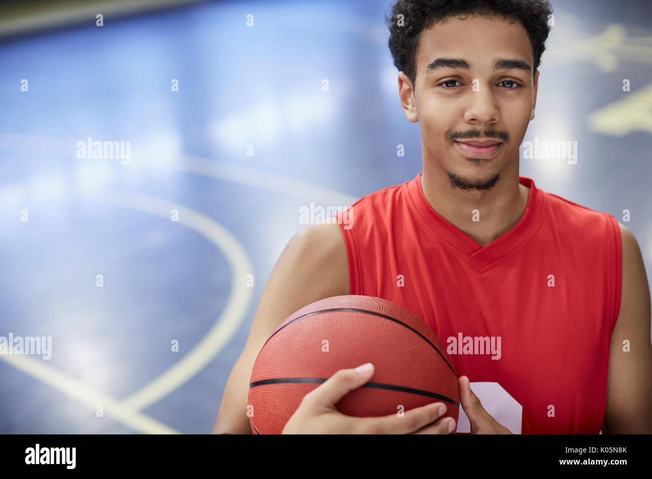 Retrato seguros macho joven jugador de baloncesto en la cancha de baloncesto de la celebración Foto de stock