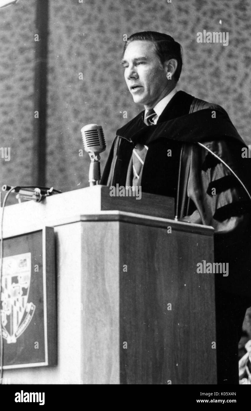 Tres cuartos de longitud retrato de un miembro de la facultad de no identificados en la Johns Hopkins 1971 Comienzo, vistiendo una túnica y de pie detrás de un podio haciendo un discurso, hablando en un micrófono de plata, ataviado con una corbata y camisa blanca, con una grave expresión facial. 1971. Foto de stock