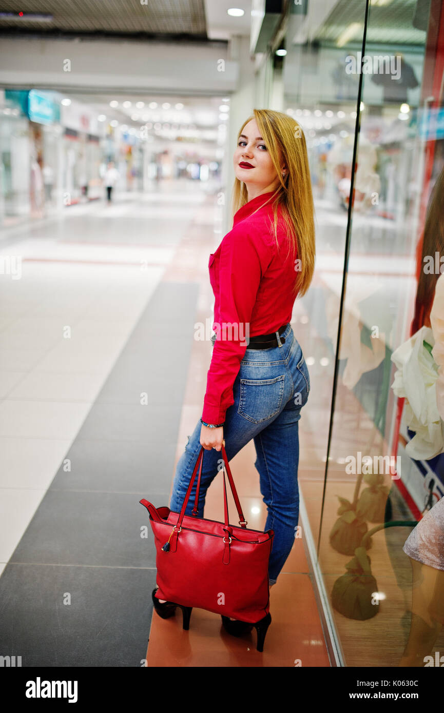 Retrato de mujer vistiendo una blusa roja, casuales jeans y zapatos de tacón negro plantea con bolso de cuero en el gigantesco centro comercial Fotografía de stock Alamy