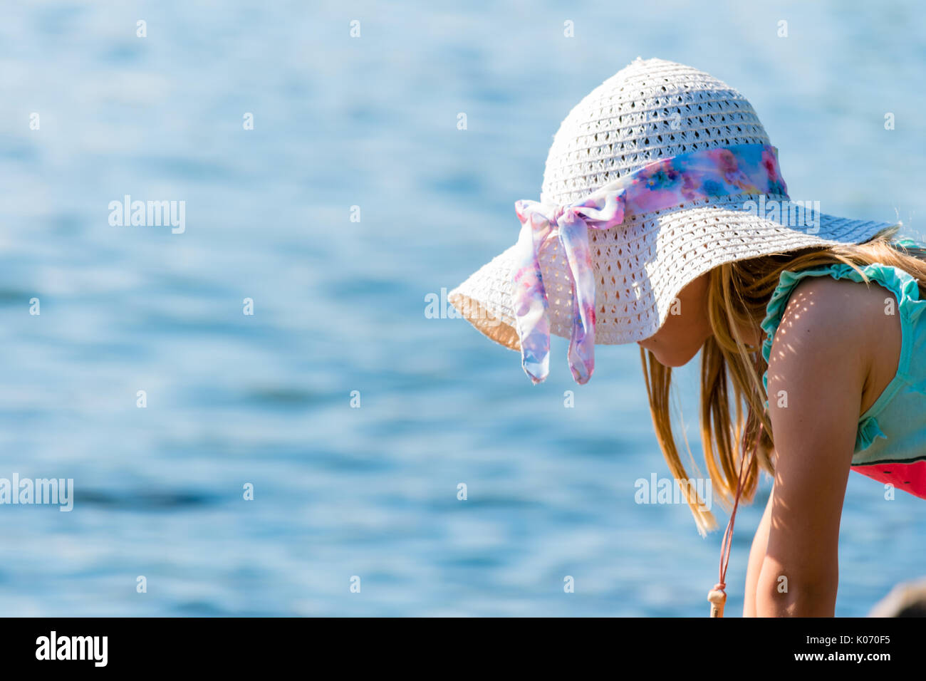 Yount hermosa chica con sombrero mirando al mar. La superficie de agua sobre fondo liso. Bonita escena soleado de verano. Foto de stock