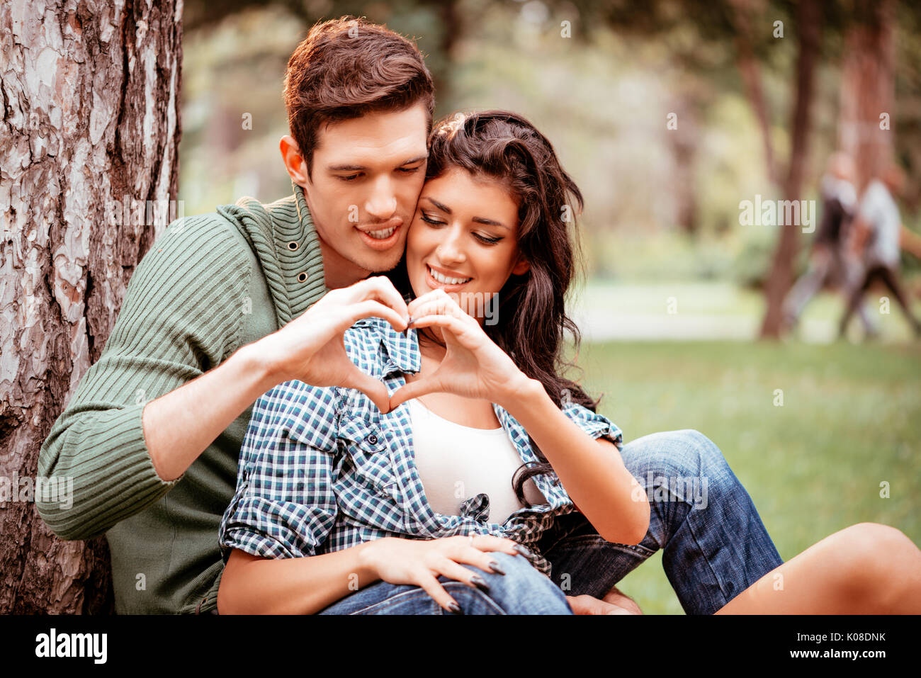 Hermosa hermosa pareja disfrutando en el parque y con sus manos haciendo una forma de corazón. Foto de stock