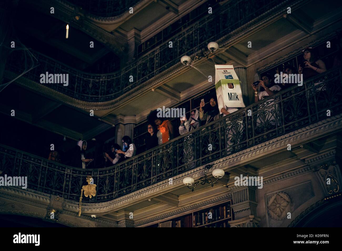 Vista de uno de los pisos superiores de la biblioteca Peabody, estudiantes universitarios están de pie mirando hacia abajo y un estudiante está vestida como una gran caja de cartón de leche, 2015. Cortesía de Eric Chen. Foto de stock