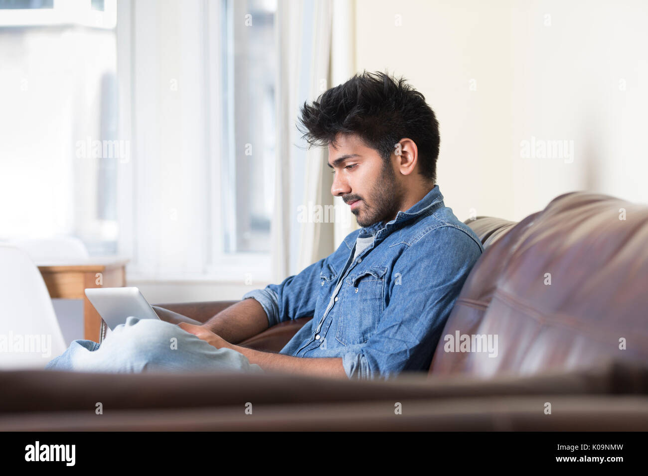 Hombre asiático mediante tableta digital en casa en el sofá. Foto de stock