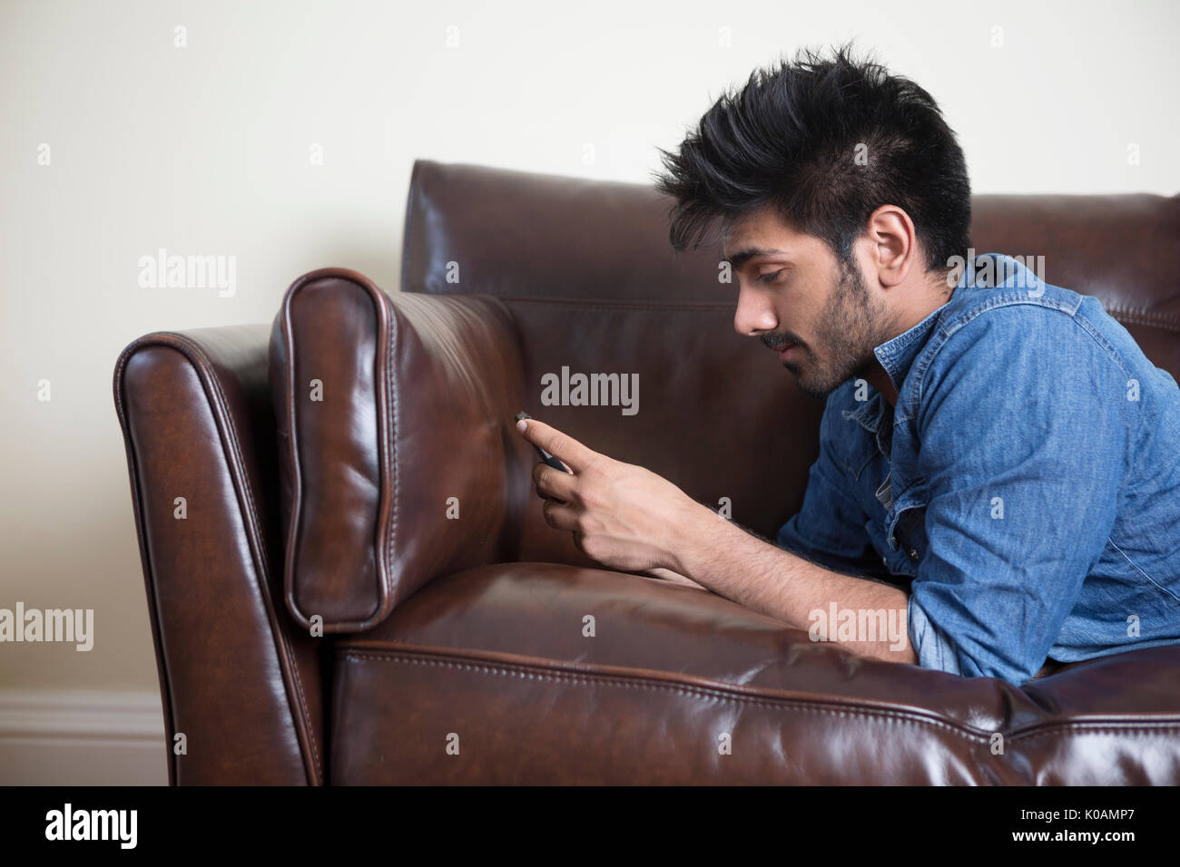 Asian tumbado en el sofá enviando un mensaje de texto Foto de stock