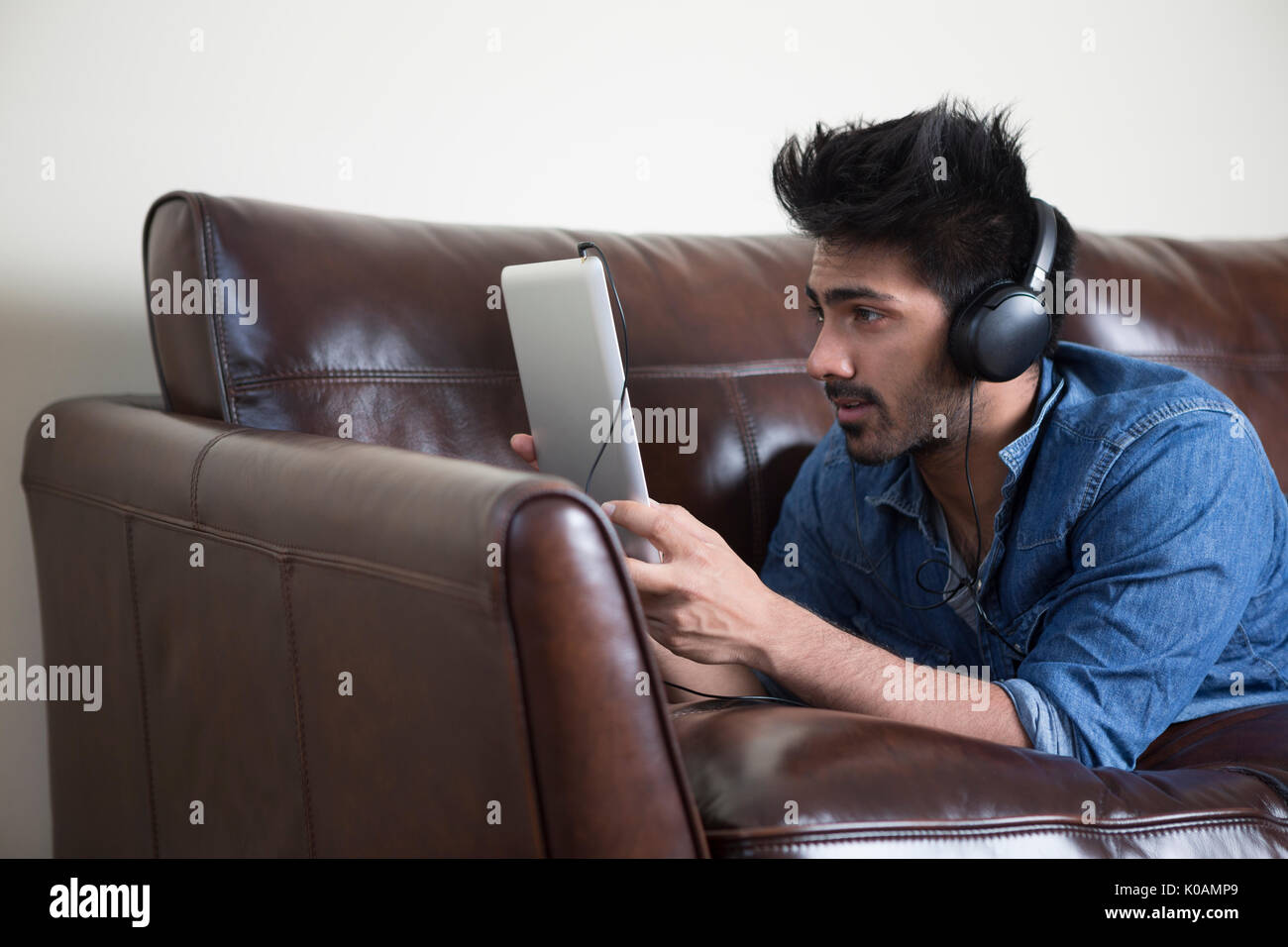 Feliz hombre asiático mediante tableta digital en casa en el sofá. Foto de stock