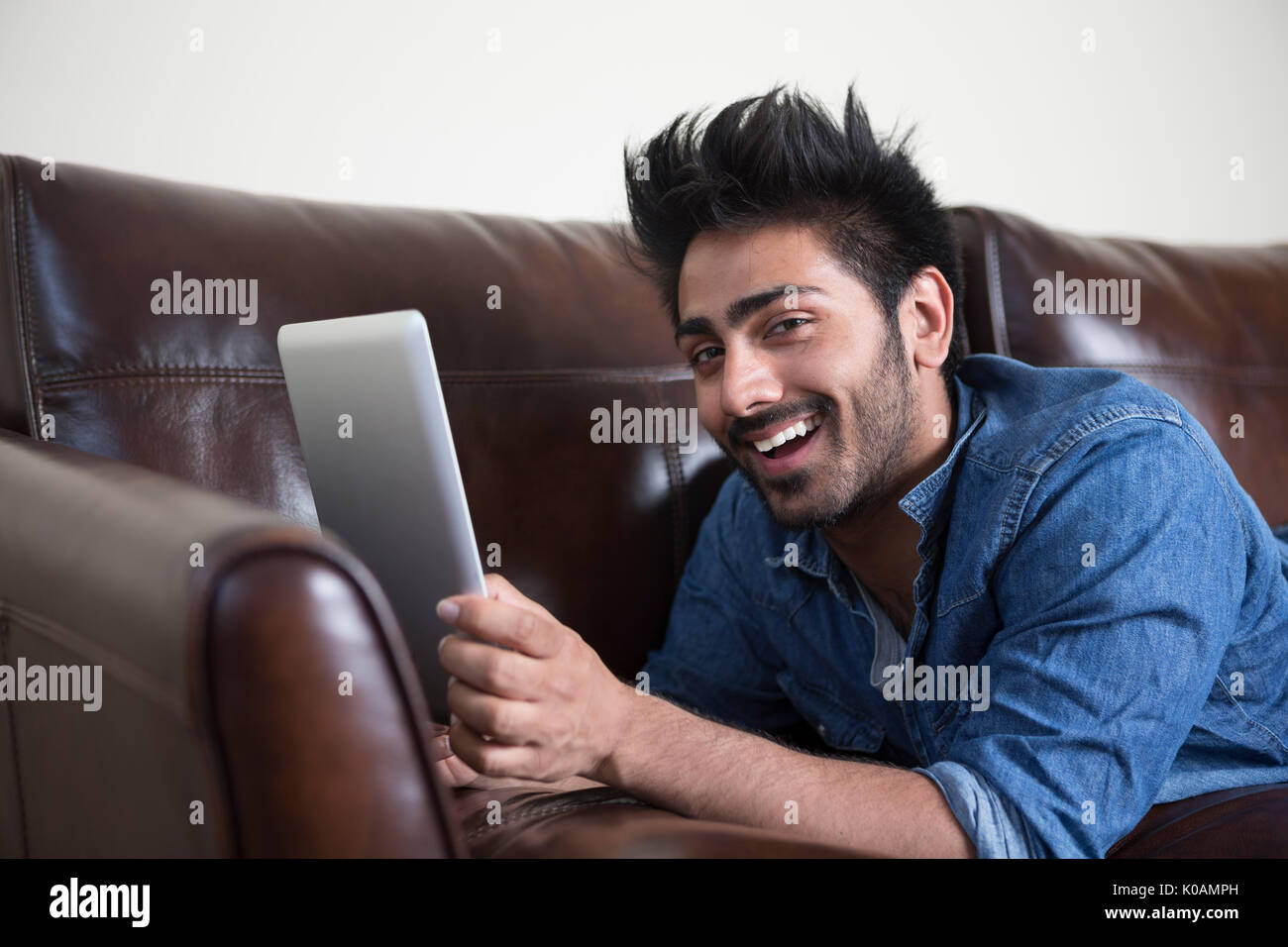 Feliz hombre asiático mediante tableta digital en casa en el sofá. Foto de stock