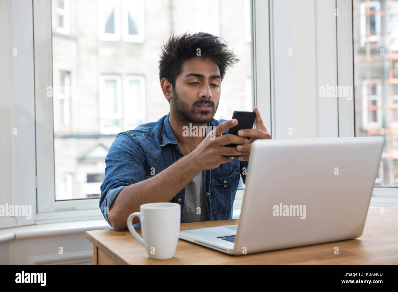 Retrato de un hombre de origen indio sentado a la mesa en casa trabajando en un ordenador portátil. Foto de stock