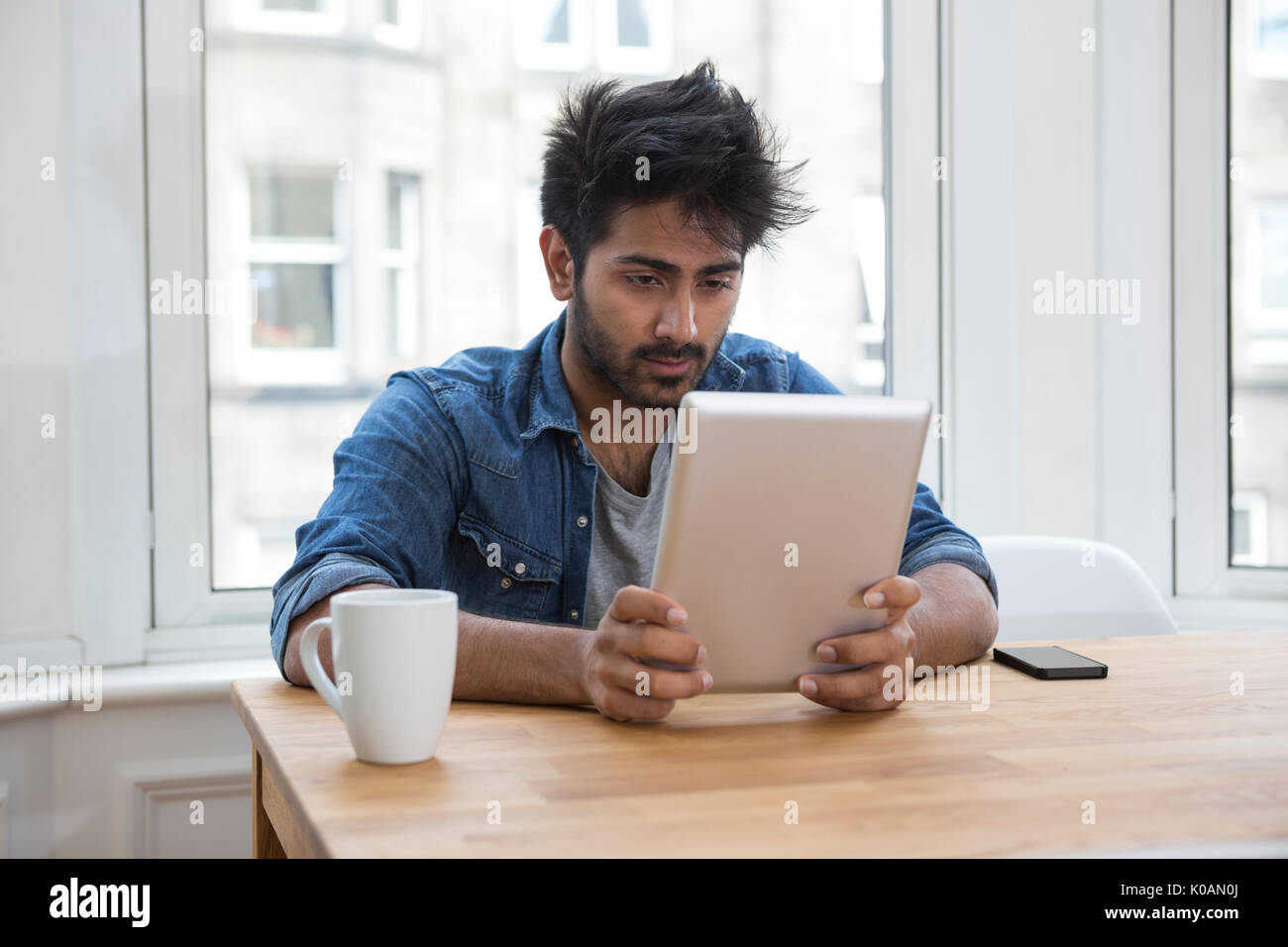 Retrato de un hombre de origen indio sentado en una mesa en la casa Leer un equipo Tablet PC. Foto de stock