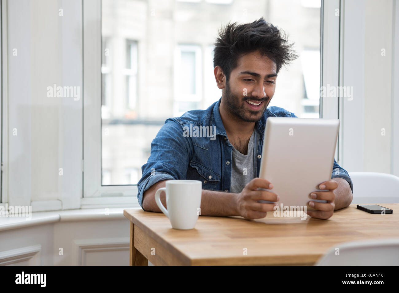 Retrato de un hombre de origen indio sentado en una mesa en la casa Leer un equipo Tablet PC. Foto de stock
