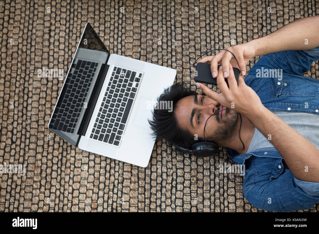 Hombre asiático tumbado en el suelo en casa con un ordenador portátil y teléfono. Vista anterior Foto de stock