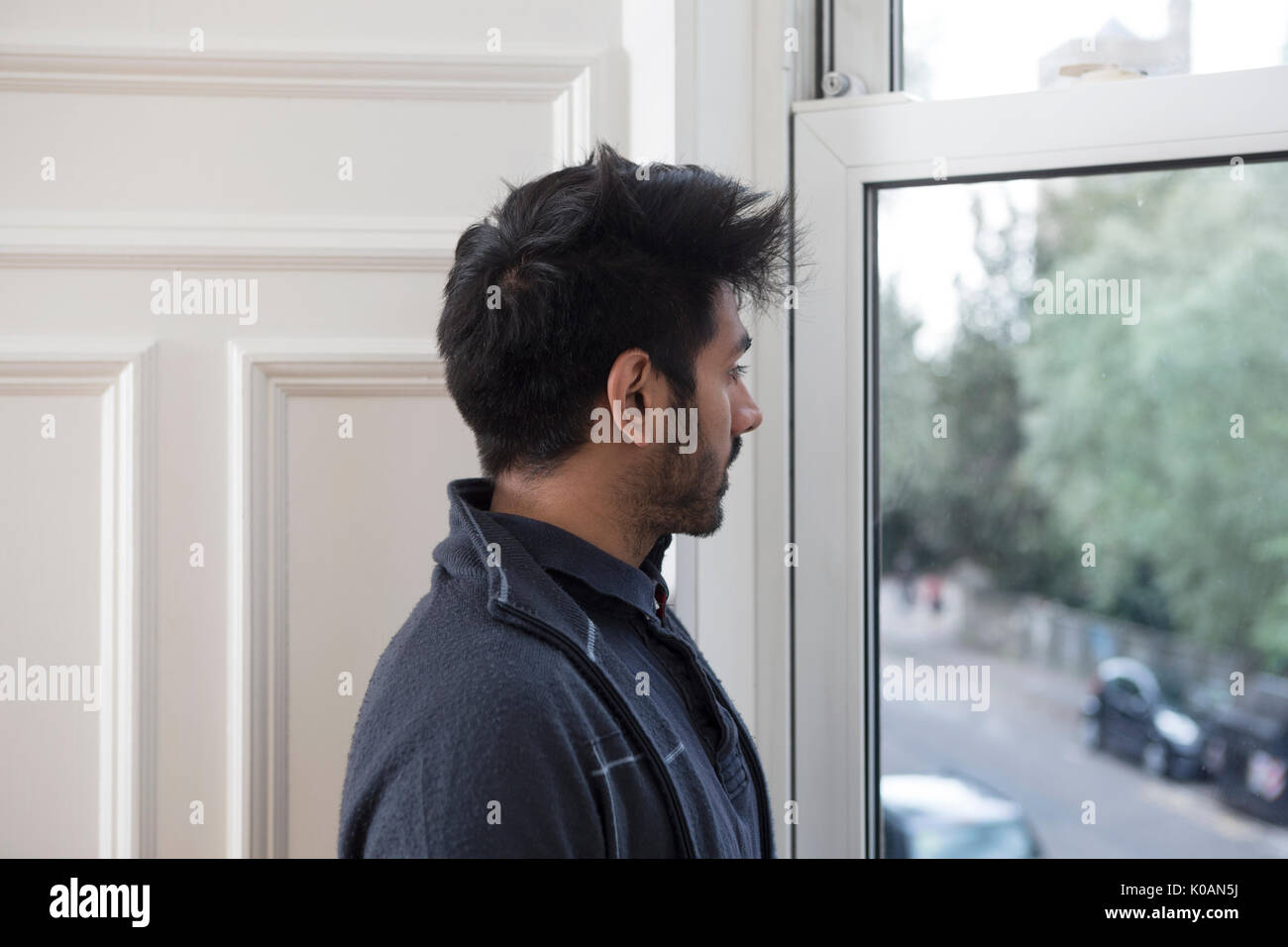 Retrato de un hombre asiático en casa mirando por la ventana. Foto de stock