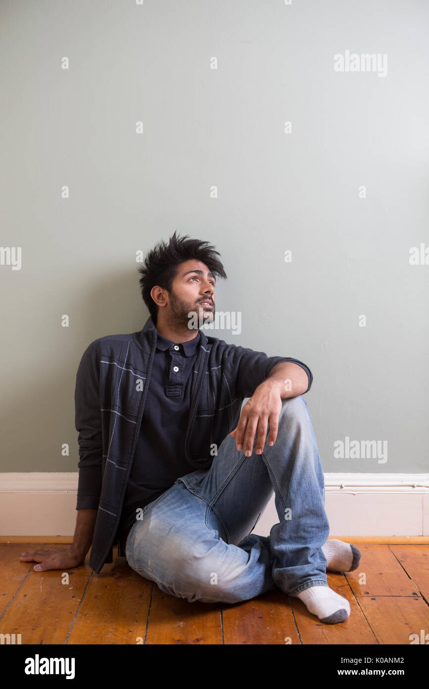 Retrato de un hombre de origen indio feliz sentada en el piso contra la pared verde. Foto de stock