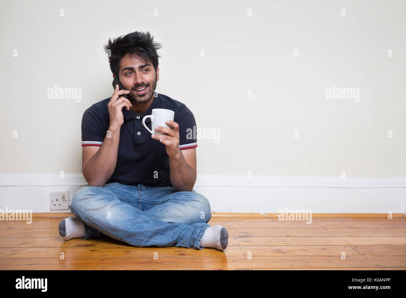 Retrato de un hombre asiático moderno sentado en el piso utilizando su teléfono. Foto de stock