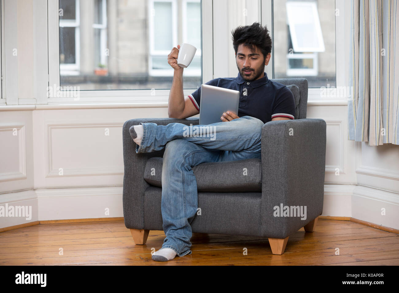 Hombre asiático mediante tableta digital en casa en el sofá. Foto de stock
